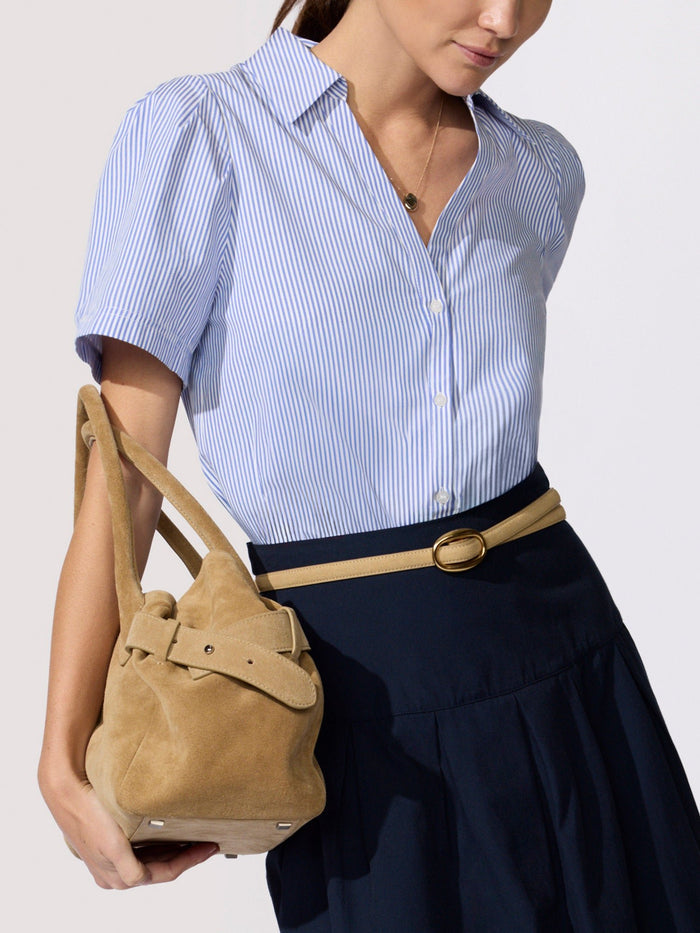 Woman wearing a blue and white striped shirt with a navy skirt, holding a tan suede bucket bag