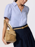 Woman wearing a blue and white striped shirt with a navy skirt, holding a tan suede bucket bag