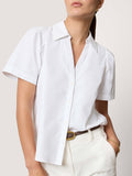 Close-up of a woman wearing a white short-sleeve button-up shirt tucked into cream trousers with a brown leather belt