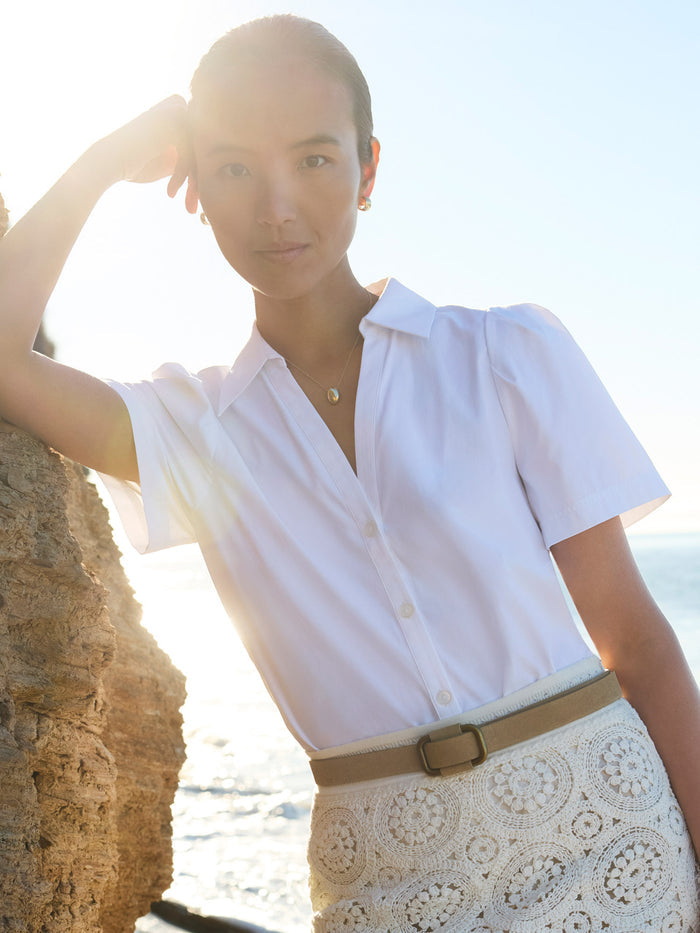 Woman wearing a white puff-sleeve blouse with a cream crochet skirt and tan belt by the beach