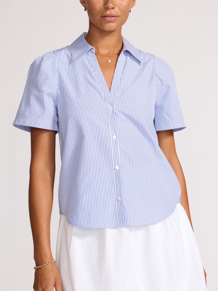 Front view of a woman wearing a buttoned-up blue and white pinstripe shirt over a white skirt