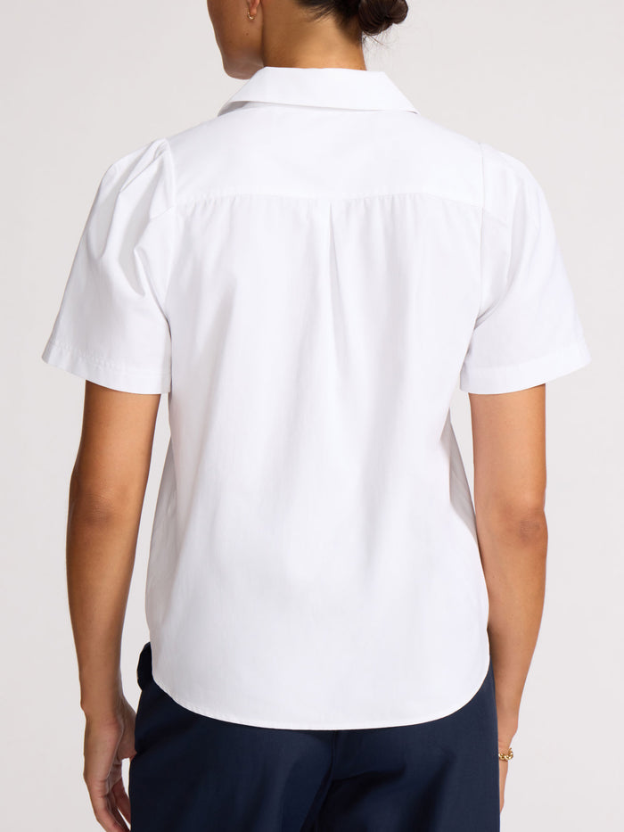 Back view of a woman wearing a white short-sleeve button-front shirt tucked into navy trousers