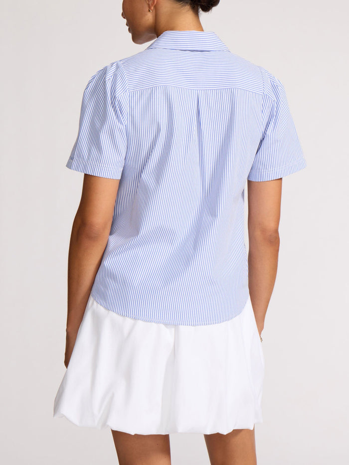 Back view of a woman wearing a blue and white pinstripe shirt over a white skirt