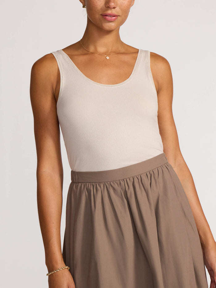 Front view of a woman wearing a cream ribbed tank top and taupe midi skirt