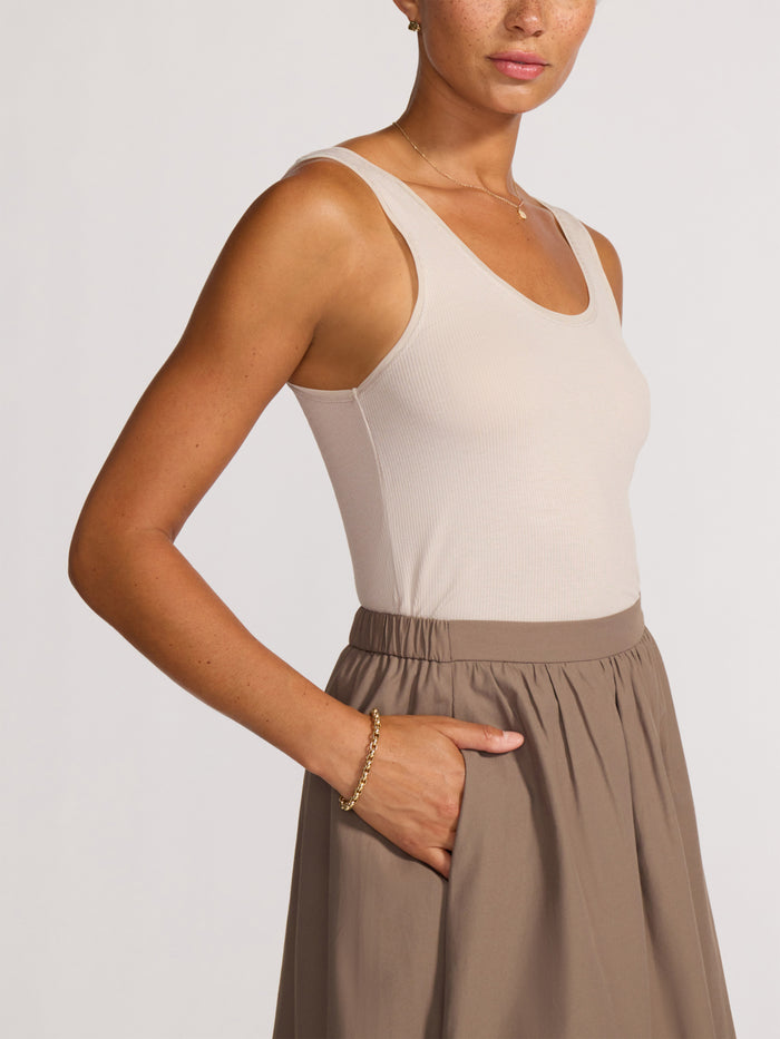 Close-up of a woman wearing a cream ribbed tank top tucked into a taupe midi skirt