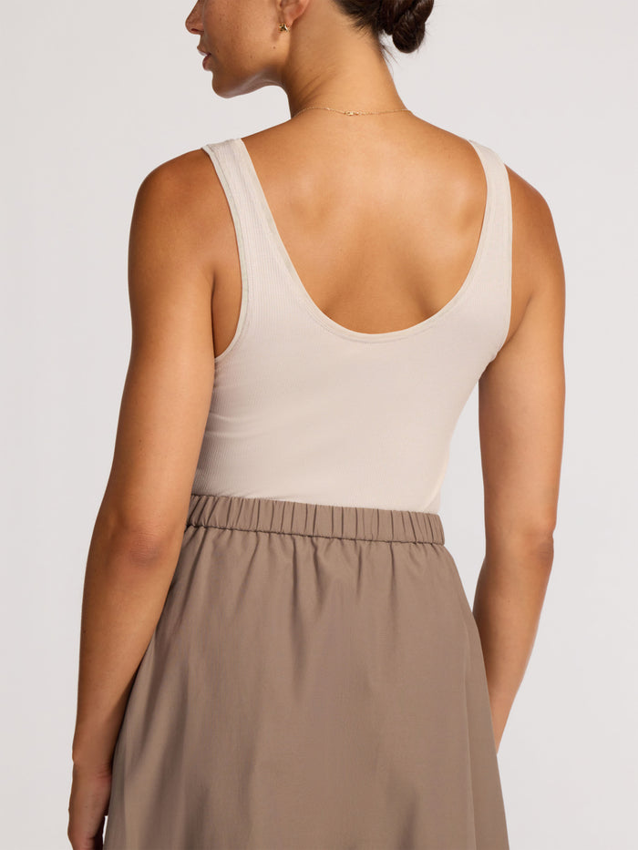 Back view of a woman wearing a cream ribbed tank top and taupe midi skirt
