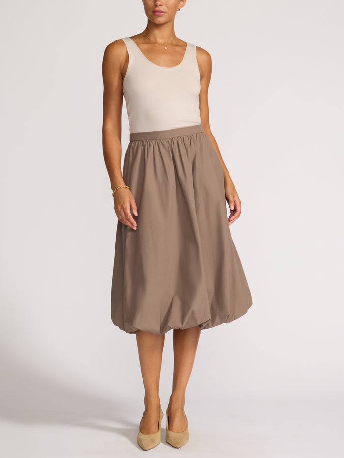 Full-length view of a woman wearing a cream tank top and taupe bubble-hem midi skirt