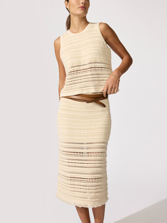 Woman wearing an ecru crochet tank top and matching crochet midi skirt with a tan belt