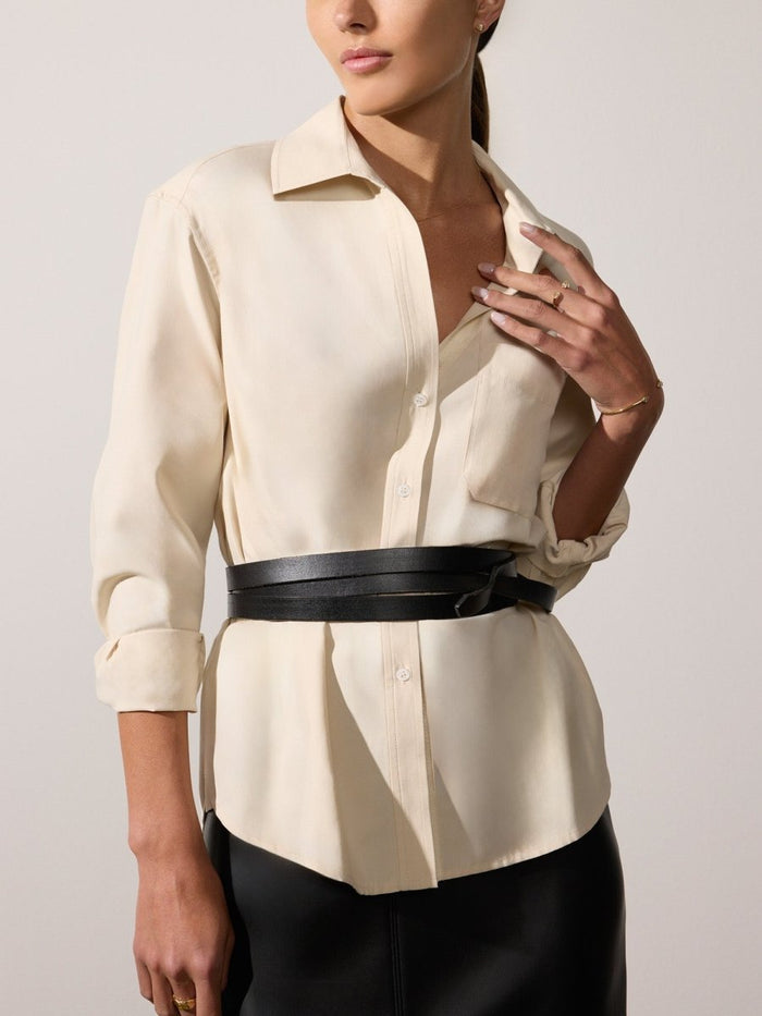 Black leather wrap belt cinched twice over an ivory button-up shirt with a black skirt.