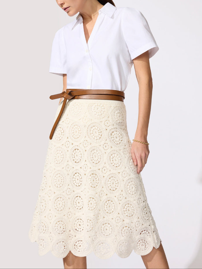 Woman wearing a white blouse with a cream crochet lace skirt and a tan leather belt