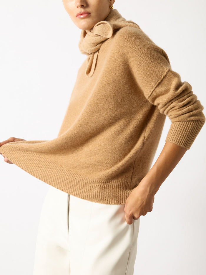 Camel cashmere neck square knotted over a tan sweater with ivory trousers.