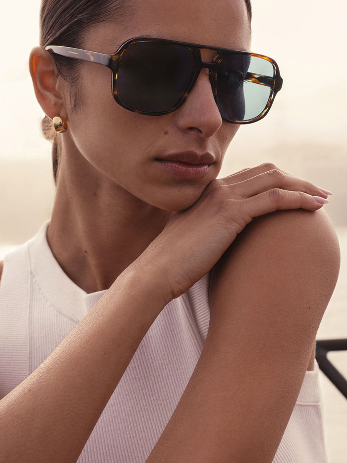 Woman wearing The Cassis Sunglasses, tortoiseshell aviator vintage sunglasses, resting her chin on her hand