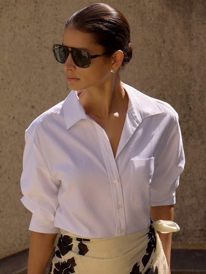 Woman wearing the Pia shirt in white with a floral print wrap skirt and sunglasses