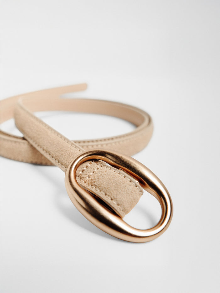 Close-up of a tan suede belt with a rose gold circular buckle