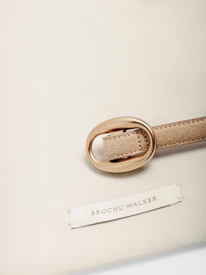 Beige suede belt with a gold buckle resting on a fabric pouch with a woven label