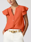 Woman wearing an orange flutter-sleeve Darya top with white pants and a tan belt