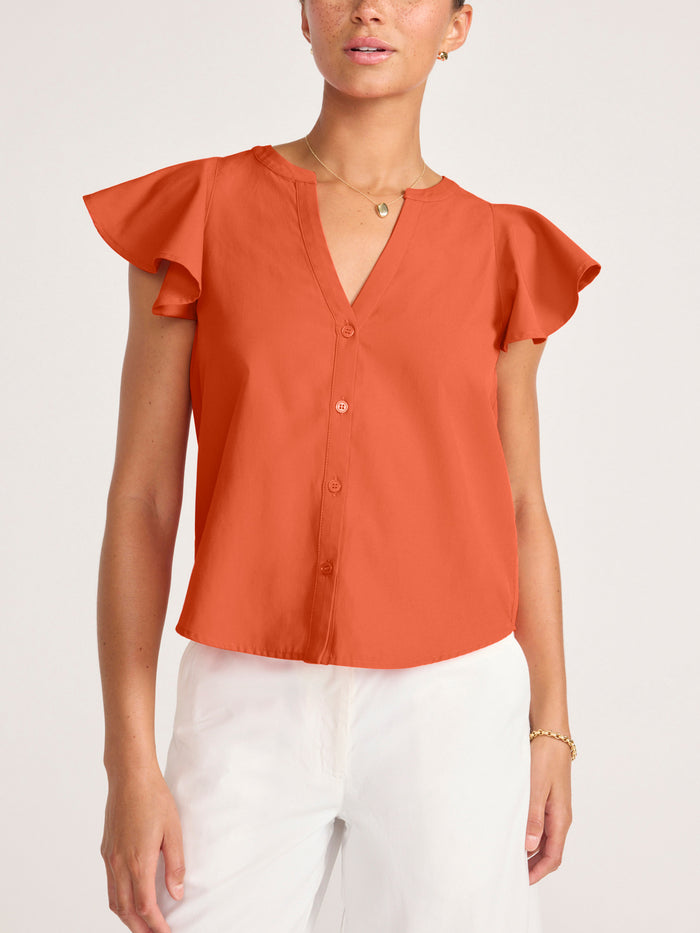 Woman wearing a rust orange ruffle-sleeve button-front blouse tucked into white pants
