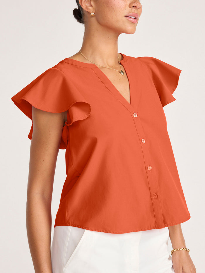 Close-up of a woman wearing a rust orange ruffle-sleeve button-front blouse with a gold necklace
