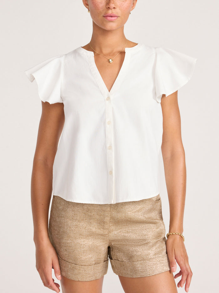 Model wearing a white ruffle-sleeve V-neck blouse with tan shorts