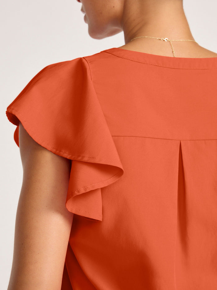 Close-up of a rust orange ruffle-sleeve blouse showing the back yoke and pleat detail on a model