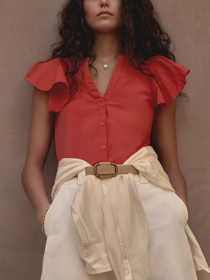 Woman wearing a coral red flutter-sleeve Darya top with a cream tie-belt skirt