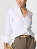 Classy white top in a crisp poplin with a spread collar, V-neckline, and long cuffed sleeves tucked into taupe trousers with a tan oval-buckle belt.