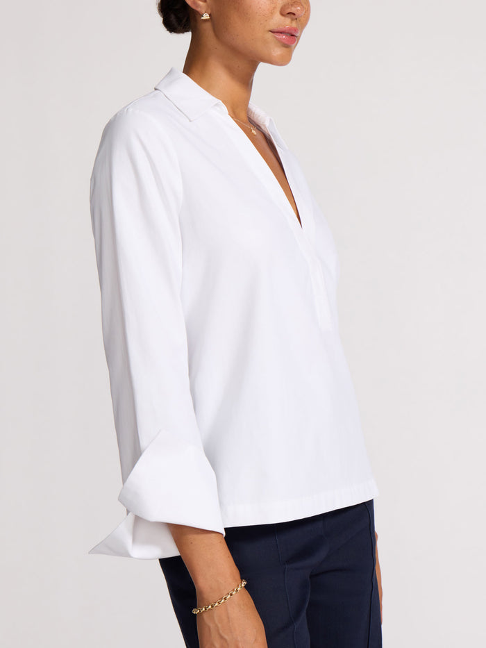 Side profile of a white v-neck popover top with a flared cuff sleeve