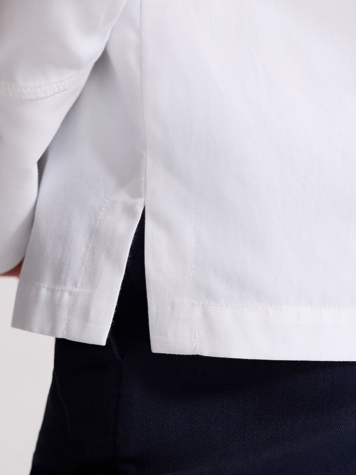 Close-up of the side hem slit on a white popover shirt worn with navy trousers
