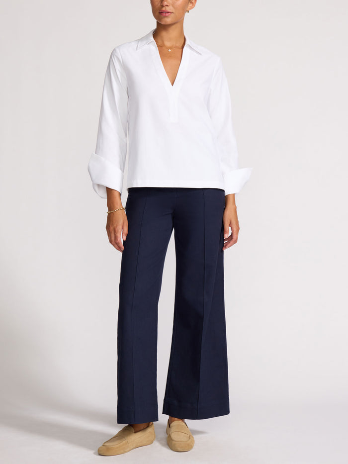 Full-length view of a woman wearing a white popover shirt with navy wide-leg trousers