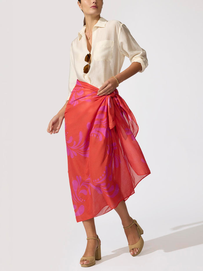 Woman wearing a cream popover shirt with an orange and pink Estara pareo tied as a wrap skirt