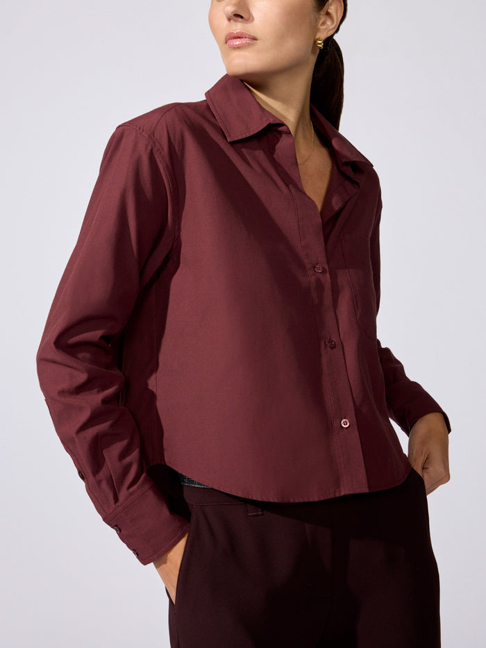 Woman wearing a maroon cropped button-up shirt with dark trousers