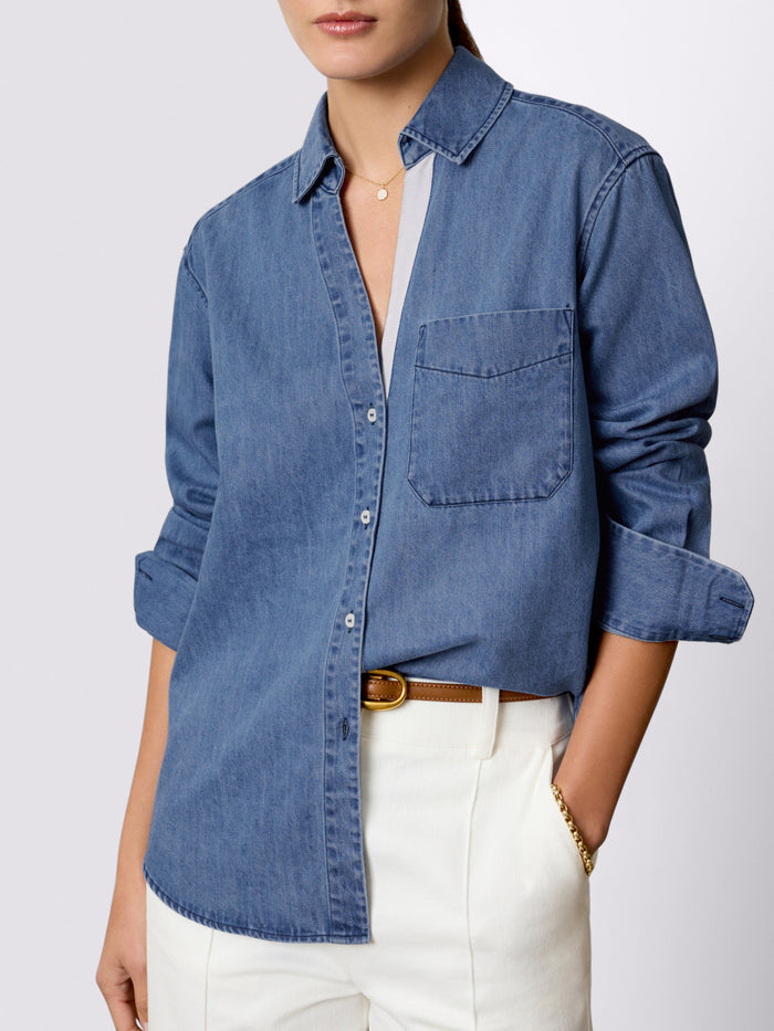 Close-up of a denim button-down shirt with a chest pocket paired with cream trousers