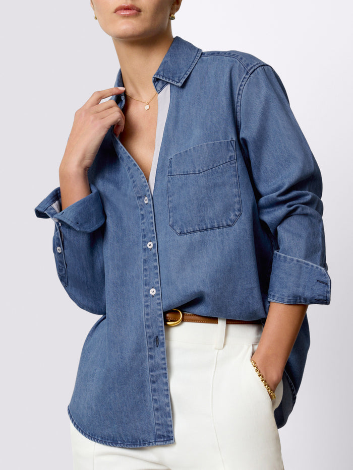 Woman wearing a classic denim button-down shirt with rolled sleeves tucked into cream trousers