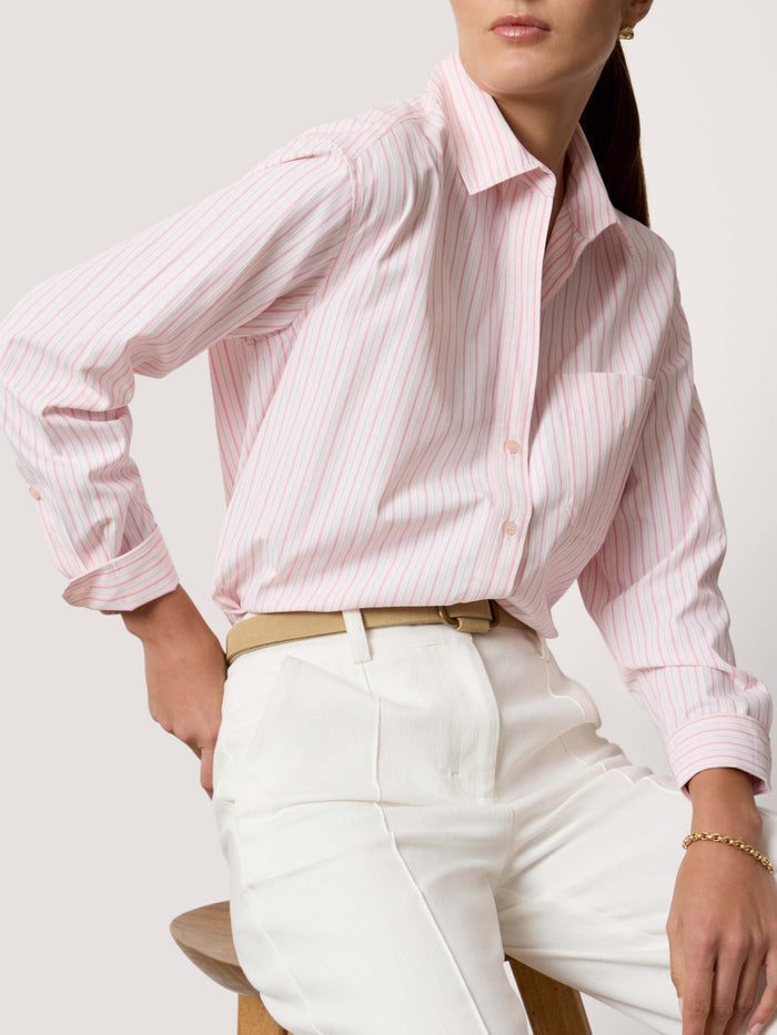 Seated woman wearing a pink striped button-down shirt with white trousers
