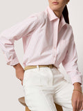 Seated woman wearing a pink striped button-down shirt with white trousers