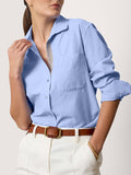 Woman wearing a light blue button-down shirt with white trousers and a brown belt