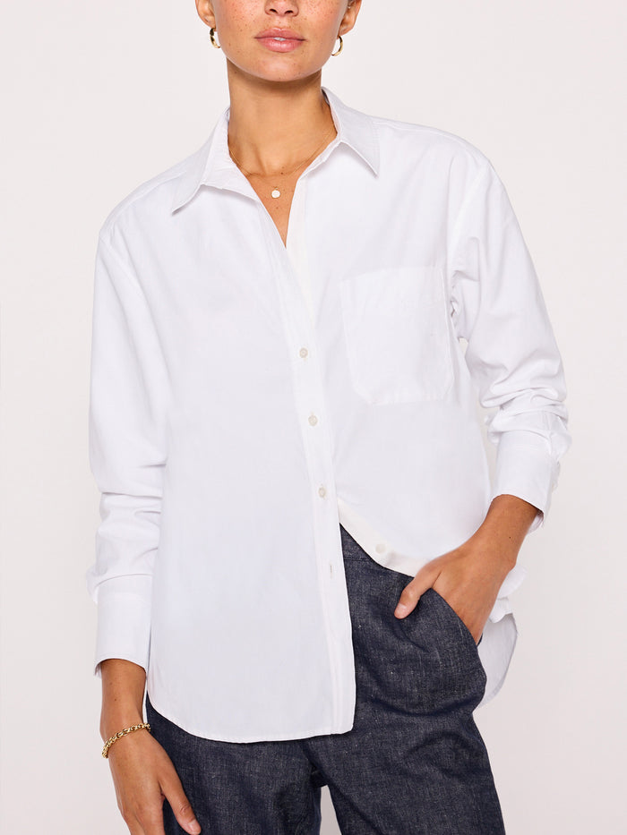 Front view of a woman wearing an oversized white button-down shirt with a denim skirt, hand in pocket