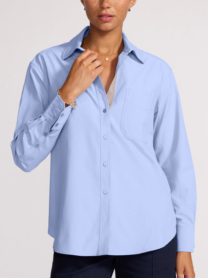 Close-up of a woman wearing an open light blue button-front shirt with a chest pocket over a beige camisole