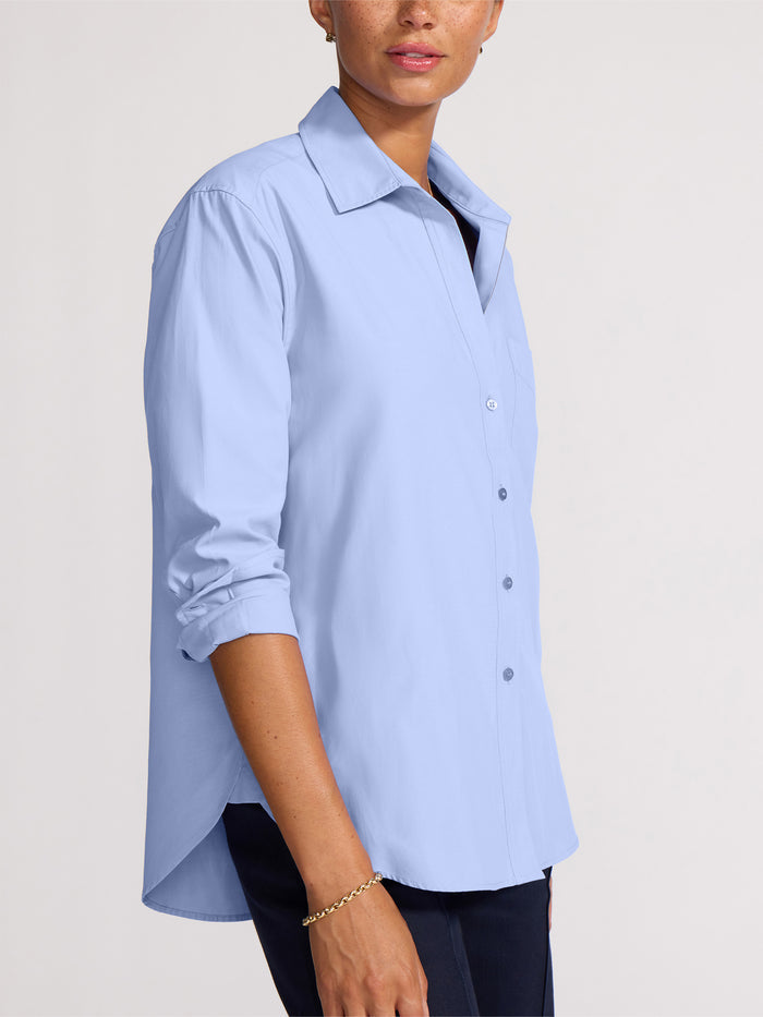 Side view of a woman wearing a buttoned-up light blue shirt tucked into navy trousers