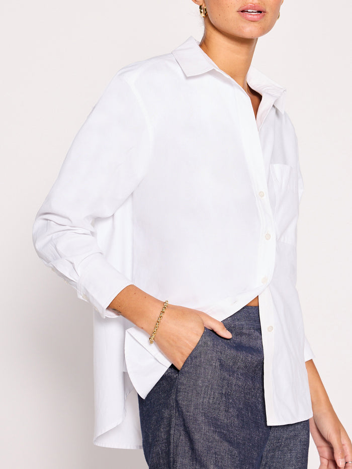 Woman wearing an oversized white button-down shirt tucked into a denim skirt, side view