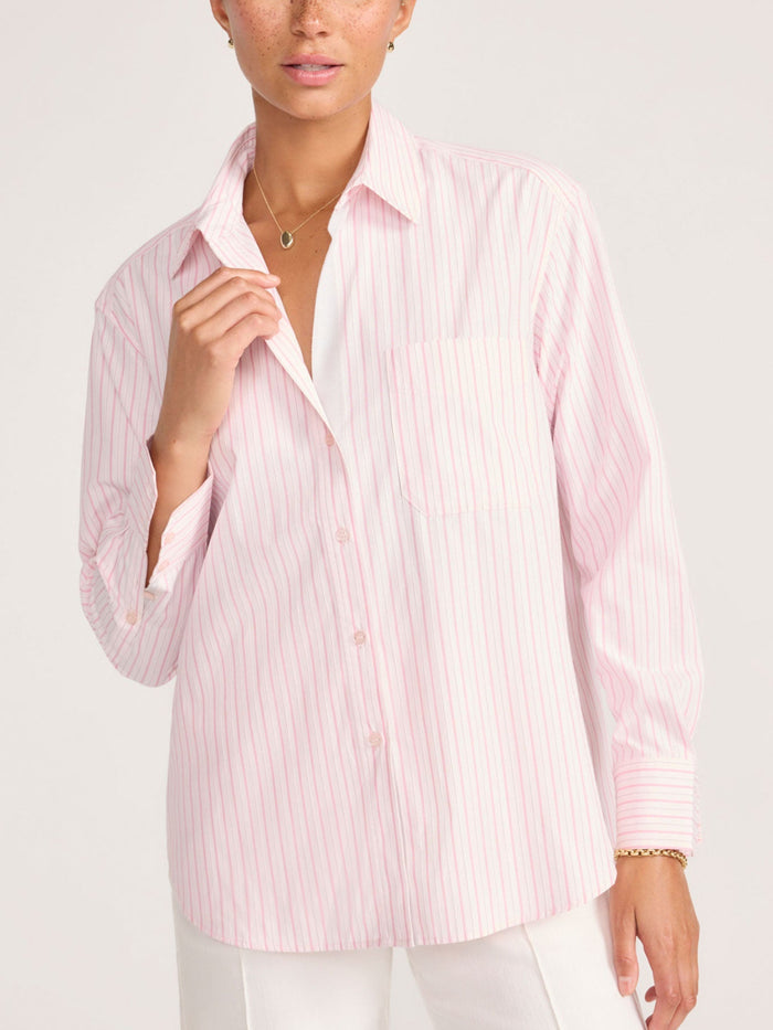 Close-up of a woman adjusting the collar of a pink and white striped button-down shirt