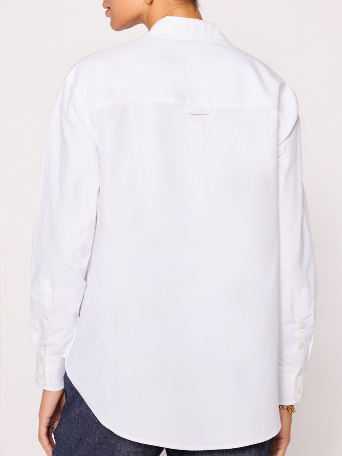 Back view of a woman wearing a white button-down shirt with long sleeves and jeans