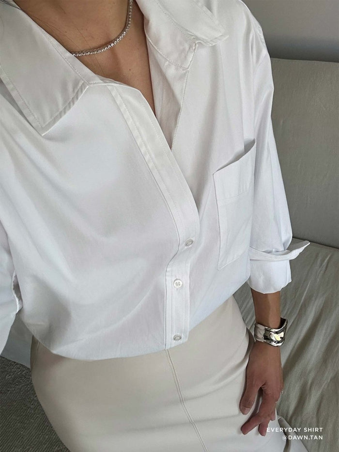 Close-up of a relaxed-fit white button-down shirt styled open at the collar with an ivory skirt.
