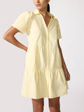 Woman wearing a pale yellow tiered button-front shirt dress with short puff sleeves.