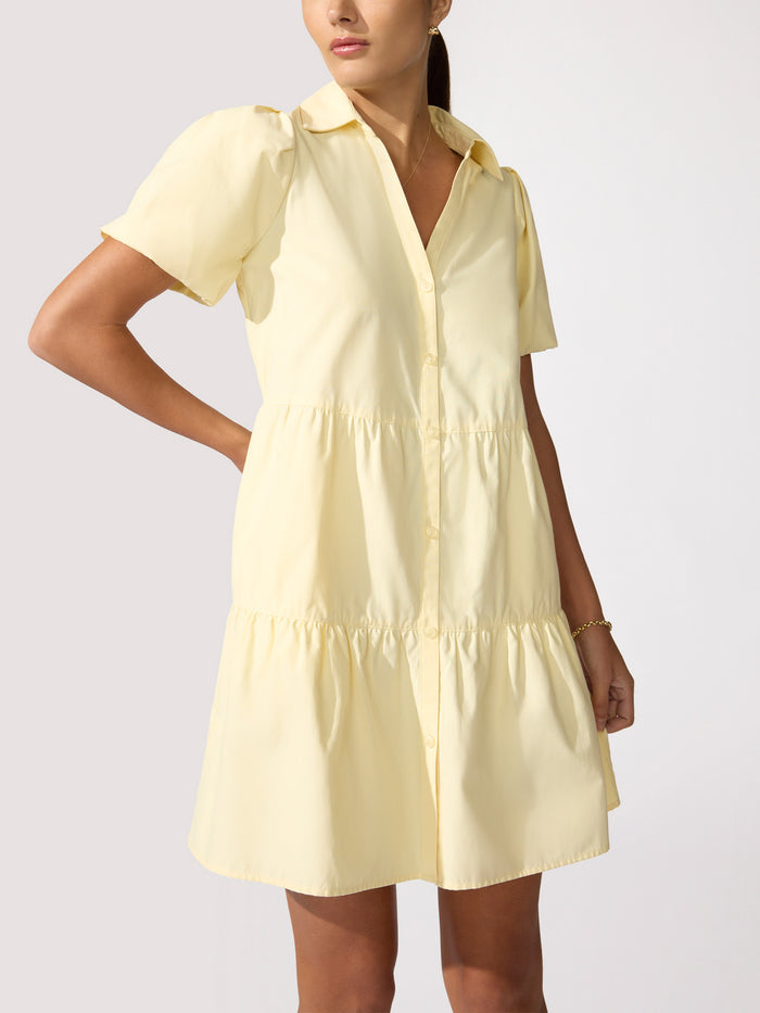 Woman wearing a pale yellow tiered button-front shirt dress with short puff sleeves.