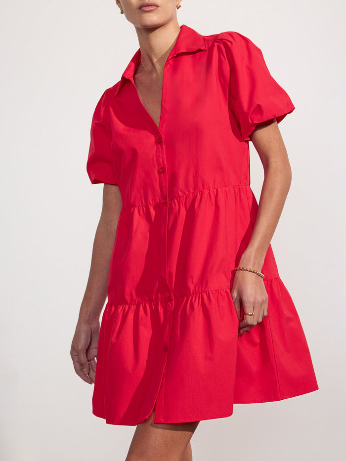 Side view of a woman wearing a red tiered mini shirtdress with puff sleeves and a collared V-neck