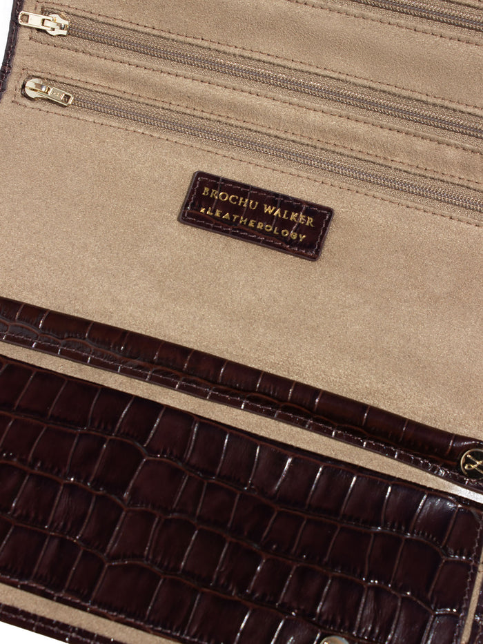 Close-up of a crocodile-embossed leather clutch interior with beige suede lining and gold-tone zippers