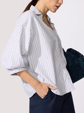 Woman wearing the Kate shirt in Riviera stripe, paired with navy trousers and a suede bag