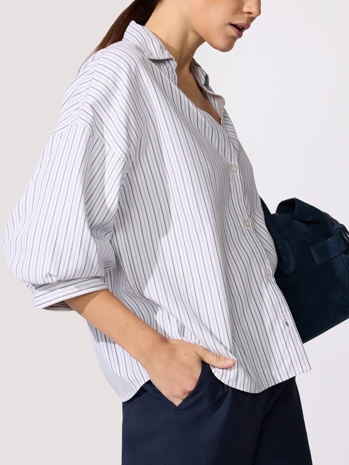 Woman wearing the Kate shirt in Riviera stripe, paired with navy trousers and a suede bag