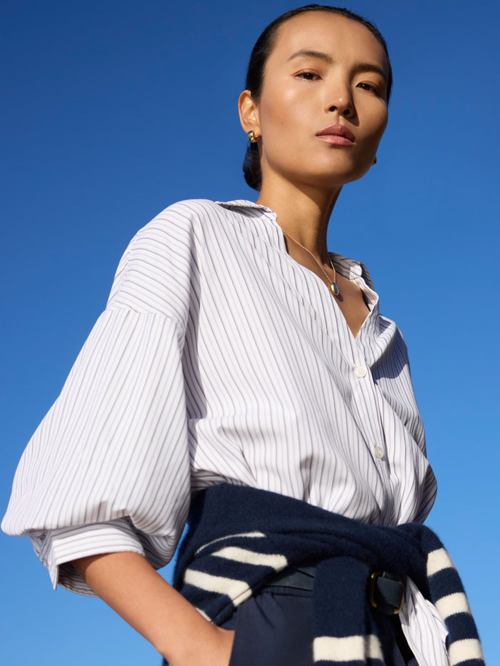 Woman in a pinstripe blouse with balloon sleeves and a sweater tied at the waist